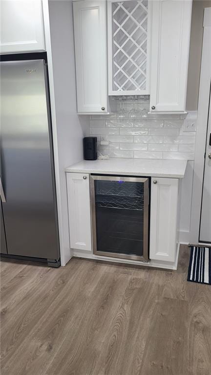 bar featuring stainless steel fridge, light hardwood / wood-style flooring, white cabinets, and beverage cooler