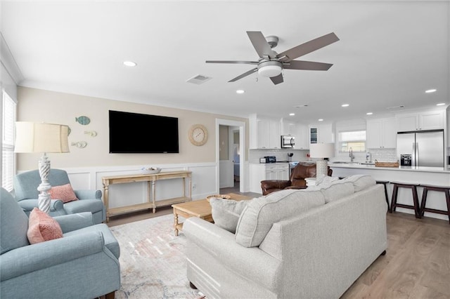 living room with ceiling fan, ornamental molding, sink, and light hardwood / wood-style flooring