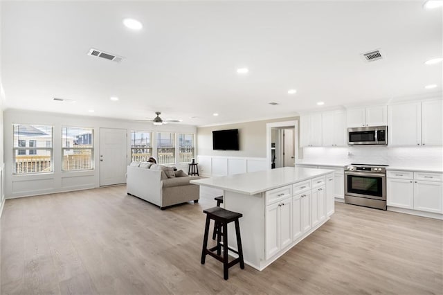 kitchen featuring white cabinets, ceiling fan, light wood-type flooring, a kitchen island, and stainless steel appliances