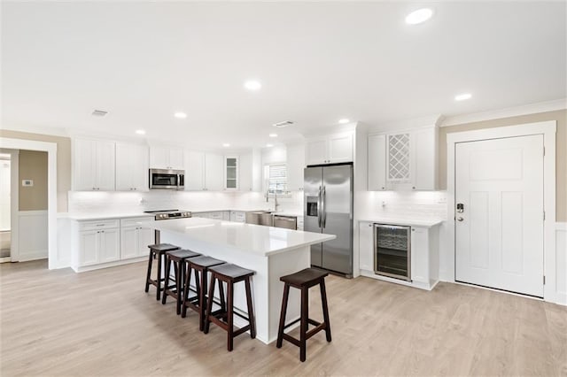 kitchen with white cabinets, appliances with stainless steel finishes, light hardwood / wood-style floors, a breakfast bar area, and beverage cooler