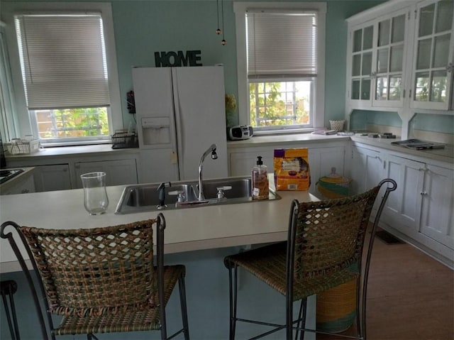 kitchen featuring a kitchen breakfast bar, wood-type flooring, white cabinetry, white refrigerator with ice dispenser, and sink