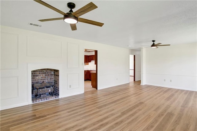 unfurnished living room featuring a fireplace, ceiling fan, and light hardwood / wood-style flooring