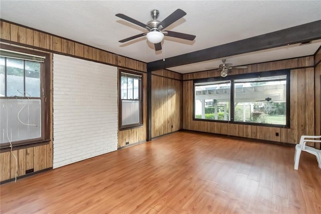 empty room featuring hardwood / wood-style floors, wood walls, ceiling fan, beam ceiling, and brick wall