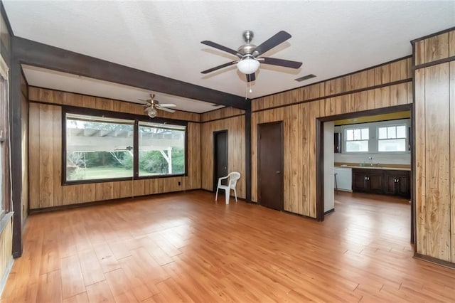 interior space with beam ceiling, ceiling fan, sink, light hardwood / wood-style flooring, and wood walls