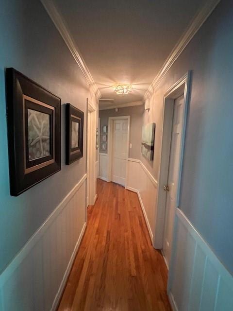 hallway with crown molding, wainscoting, light wood-type flooring, and a decorative wall