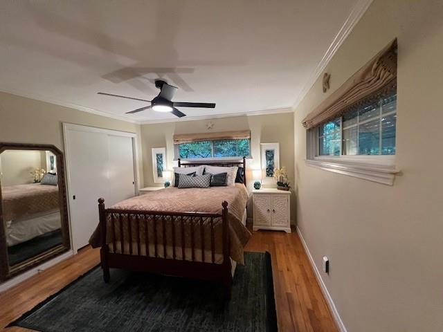 bedroom featuring crown molding, a ceiling fan, baseboards, wood finished floors, and a closet