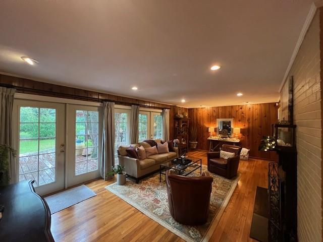 living room featuring crown molding, light wood-style floors, wood walls, french doors, and recessed lighting