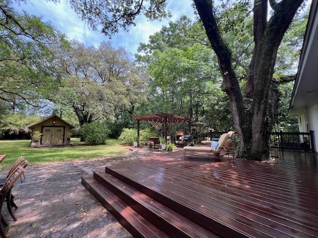 wooden terrace featuring an outdoor structure, a pergola, a shed, and a lawn