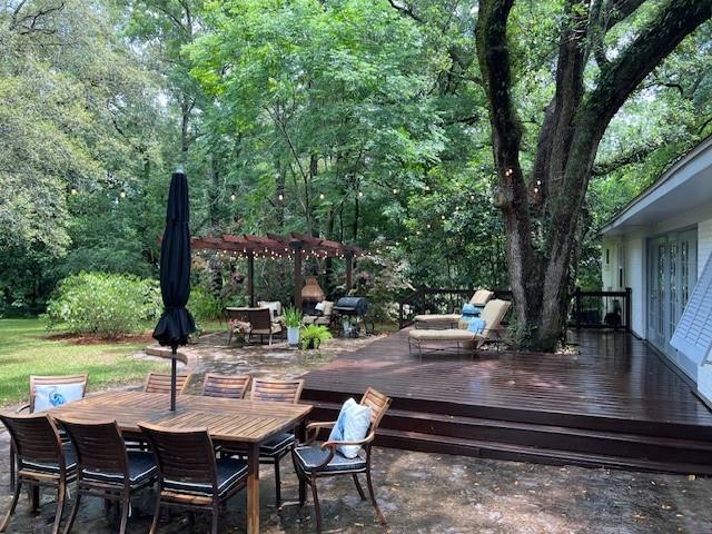 wooden deck with outdoor dining area, a wooded view, and a grill