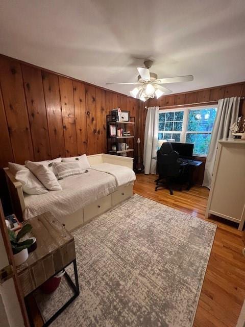 bedroom with a ceiling fan, wood walls, and light wood-style flooring