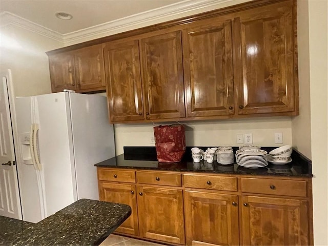 kitchen with dark stone countertops, crown molding, white fridge with ice dispenser, and light tile patterned flooring