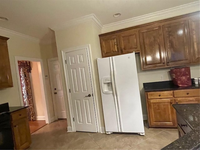 kitchen with light tile patterned flooring, ornamental molding, dark stone countertops, and white fridge with ice dispenser