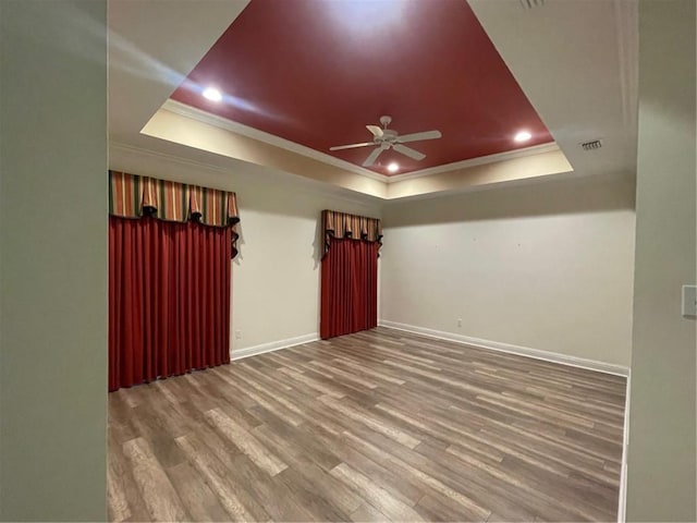 empty room with crown molding, a tray ceiling, wood-type flooring, and ceiling fan