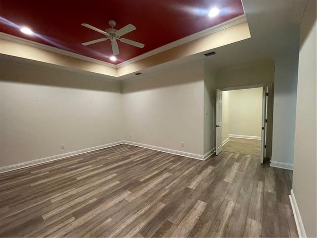 unfurnished room featuring a tray ceiling, dark wood-type flooring, ornamental molding, and ceiling fan