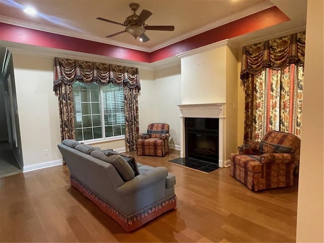 living room featuring a raised ceiling, wood-type flooring, crown molding, and ceiling fan