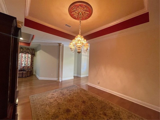 unfurnished dining area featuring crown molding, hardwood / wood-style floors, decorative columns, and a notable chandelier