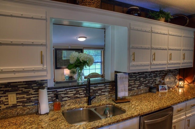 kitchen with light stone countertops, a sink, white cabinetry, backsplash, and dishwasher