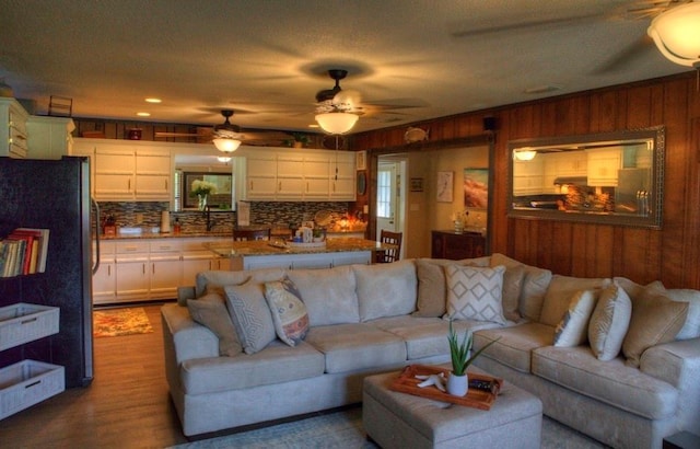 living room with wooden walls, ceiling fan, and wood finished floors