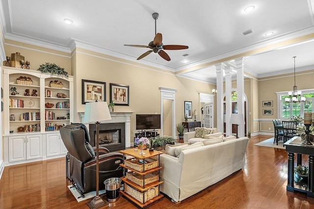 living room with decorative columns, wood-type flooring, ceiling fan with notable chandelier, and crown molding