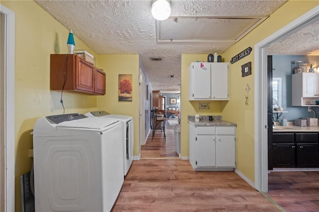 laundry area featuring cabinets, light wood-type flooring, a textured ceiling, and washing machine and clothes dryer