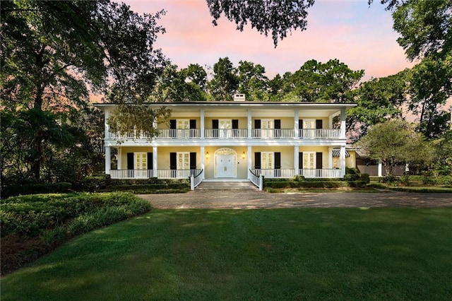 neoclassical home featuring a yard, a balcony, and covered porch