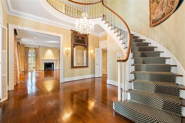 stairs with a high ceiling, a notable chandelier, a fireplace, ornamental molding, and hardwood / wood-style flooring