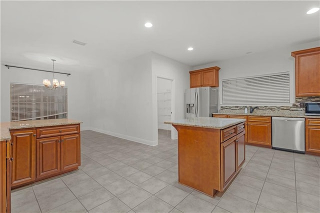 kitchen with hanging light fixtures, a center island, an inviting chandelier, appliances with stainless steel finishes, and light stone counters