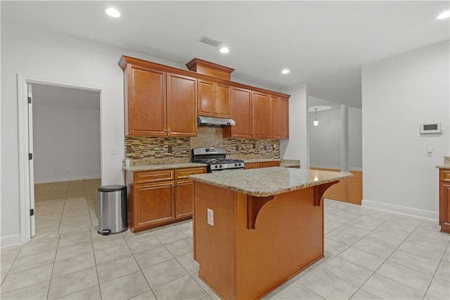 kitchen with gas stove, a breakfast bar area, backsplash, a kitchen island, and light stone countertops