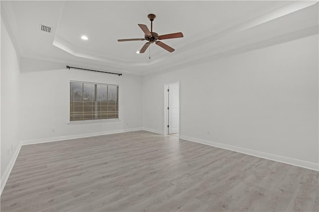 spare room with a tray ceiling, light wood-type flooring, and ceiling fan