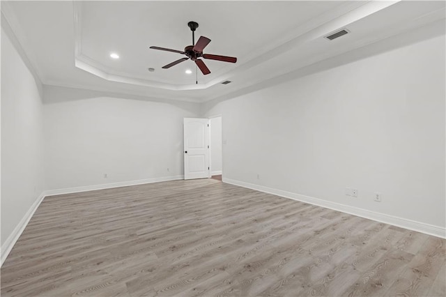 empty room featuring ceiling fan, light wood-type flooring, and a raised ceiling