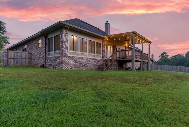 back house at dusk featuring a yard, a deck, and a sunroom