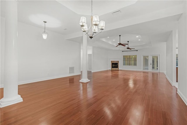 unfurnished living room featuring ornate columns, hardwood / wood-style flooring, ceiling fan with notable chandelier, and a raised ceiling