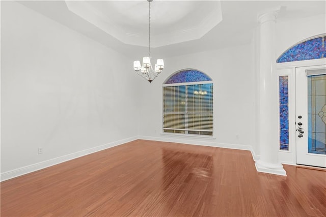 interior space featuring an inviting chandelier, hardwood / wood-style flooring, a tray ceiling, and ornate columns