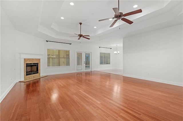 unfurnished living room featuring ceiling fan with notable chandelier, a tray ceiling, light hardwood / wood-style flooring, and a fireplace