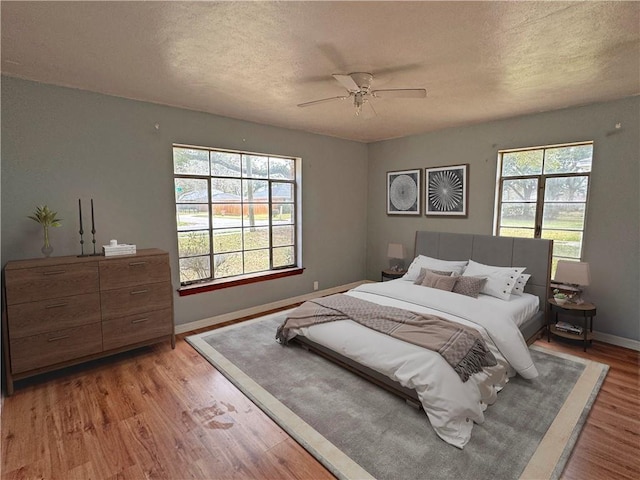 bedroom featuring a textured ceiling, light wood-type flooring, a ceiling fan, and baseboards