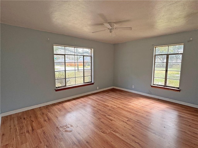 unfurnished room featuring baseboards, a textured ceiling, wood finished floors, and a healthy amount of sunlight