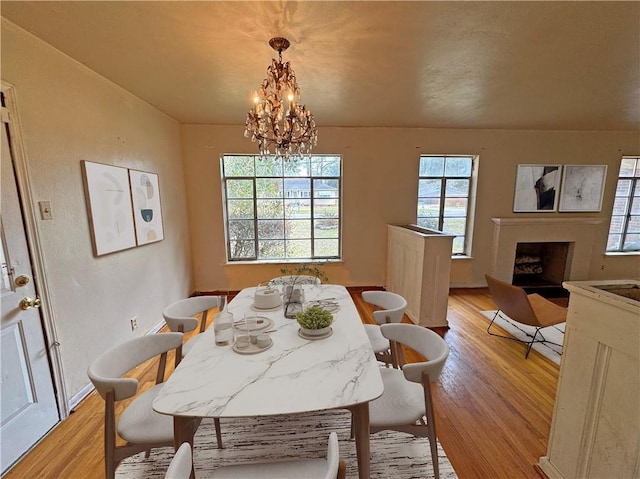 dining area with baseboards, a fireplace, light wood finished floors, and an inviting chandelier