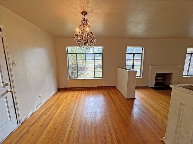 interior space featuring light wood-style floors, a fireplace, baseboards, and a notable chandelier