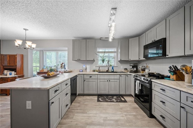 kitchen with decorative light fixtures, light countertops, gray cabinetry, black appliances, and a sink