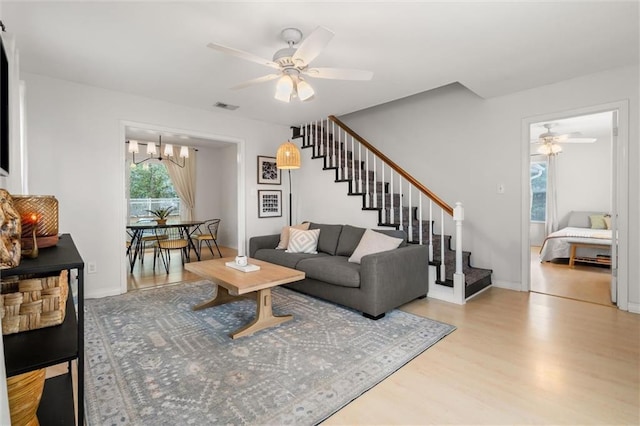 living room with ceiling fan with notable chandelier and light hardwood / wood-style flooring