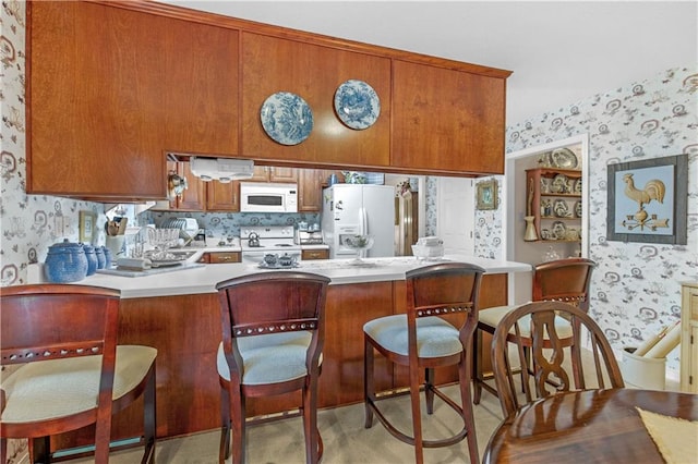 kitchen featuring kitchen peninsula, white appliances, light carpet, and a breakfast bar