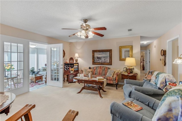 living room featuring ceiling fan, light carpet, and a textured ceiling