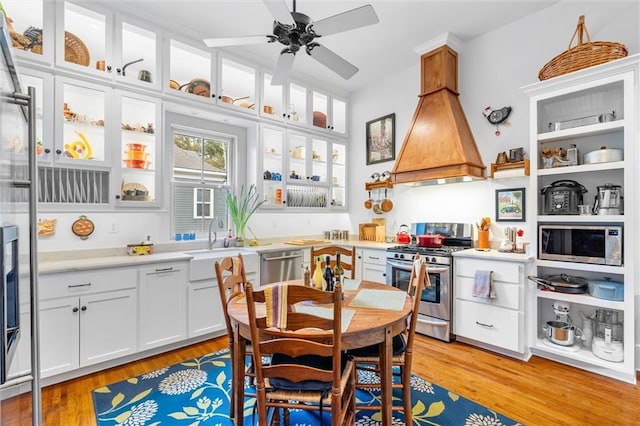 interior space featuring light hardwood / wood-style floors, custom exhaust hood, white cabinetry, and appliances with stainless steel finishes