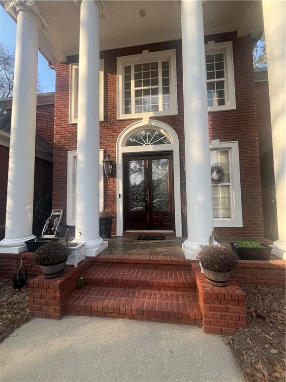 property entrance featuring brick siding, french doors, and covered porch