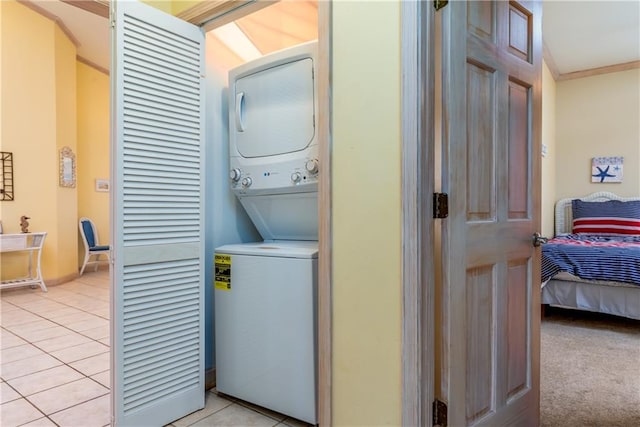 clothes washing area with light tile patterned floors, crown molding, and stacked washer and clothes dryer