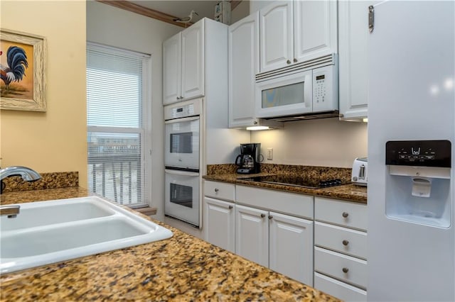 kitchen featuring white appliances, dark stone counters, sink, ornamental molding, and white cabinetry