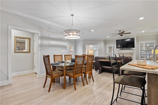 dining space with plenty of natural light, ceiling fan with notable chandelier, a tiled fireplace, light hardwood / wood-style flooring, and ornamental molding