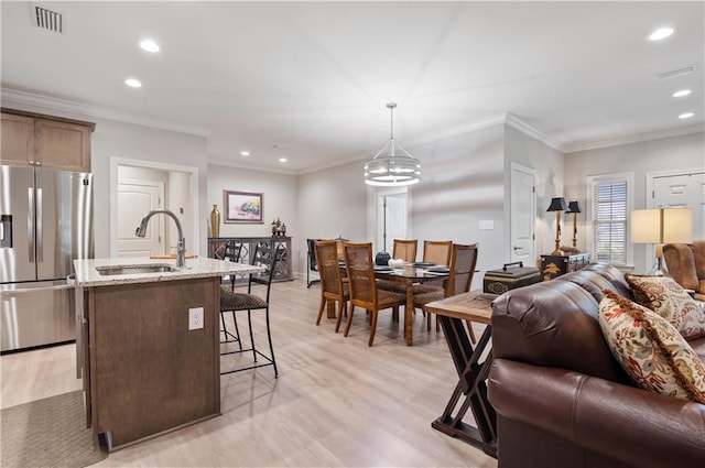 kitchen with sink, stainless steel refrigerator with ice dispenser, hanging light fixtures, light hardwood / wood-style flooring, and light stone countertops