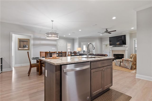 kitchen with light stone counters, sink, dishwasher, a tile fireplace, and ceiling fan with notable chandelier