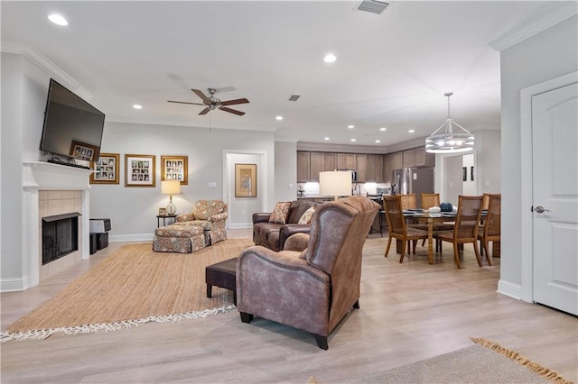 living room with ceiling fan with notable chandelier, a fireplace, ornamental molding, and light hardwood / wood-style flooring